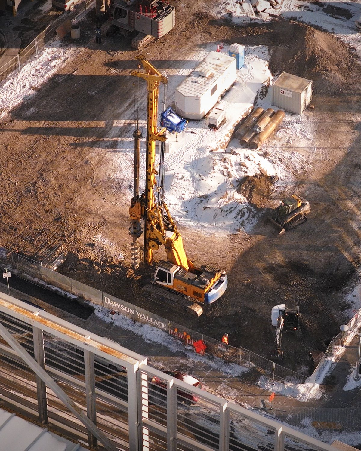 Aerial progress view of a Calgary construction site with a drill rig and site trailers